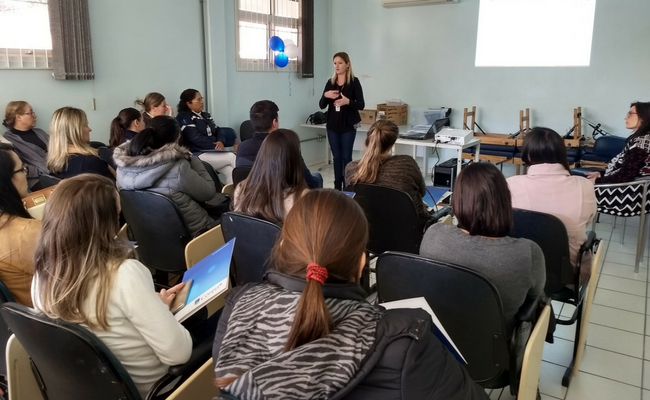 Professora em pé no fundo da sala e os alunos sentados