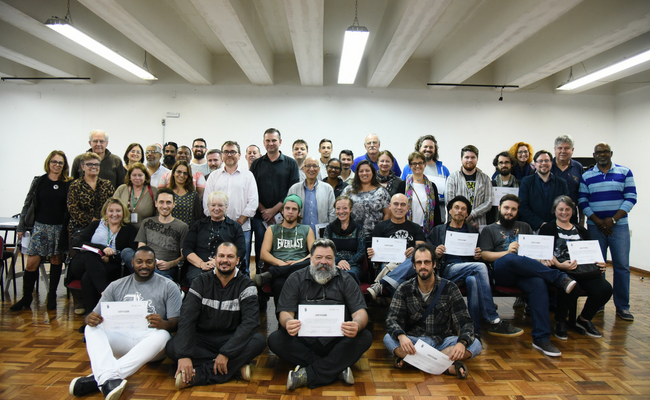 Grupo de conselheiros, uns sentandos no chão e outros em pé, segurando o diploma de posse