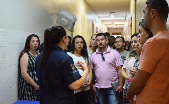 Enfermeira em pé fala para um grupo de pessoas também em pé