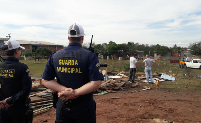 Dois policiais em pé no primeiro plano e equipe da Diretoria de Habitação ao fundo realizando a ação