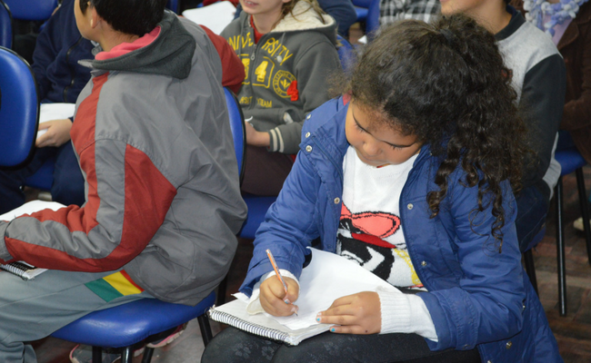 Menina sentada em uma cadeira escrevendo em um caderno no colo
