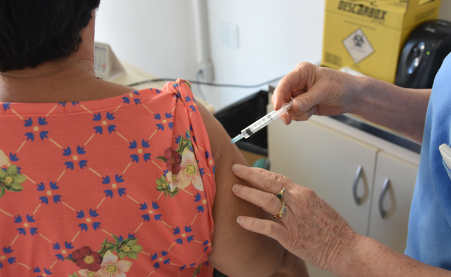 Uma paciente em pé e a enfermeira também em pé aplicando uma vacina