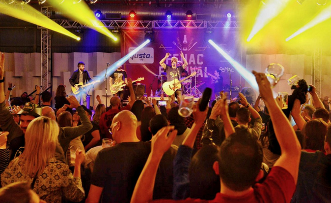 Palco ao fundo com a banda tocando e o público de costas