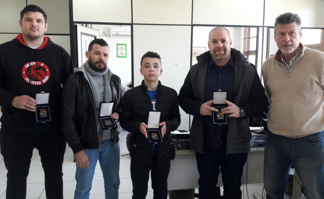 Atletas seguram a medalha em pé, com o secretário Jorginho ao lado