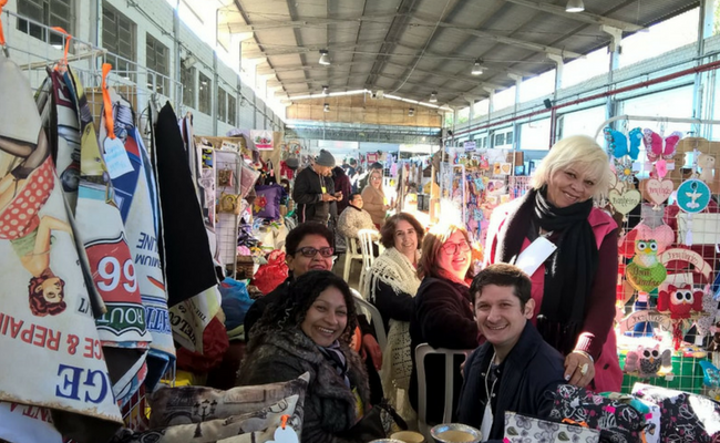 Grande pavilhão, com produtos expostos e quatro pessoas à frente 