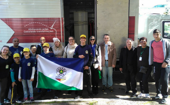 Ao lado de um caminhão, pessoas em pé lado a lado uma das outras posam para a foto