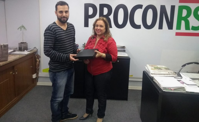 Lucas em pé recebe da Diretora Maria o tablet