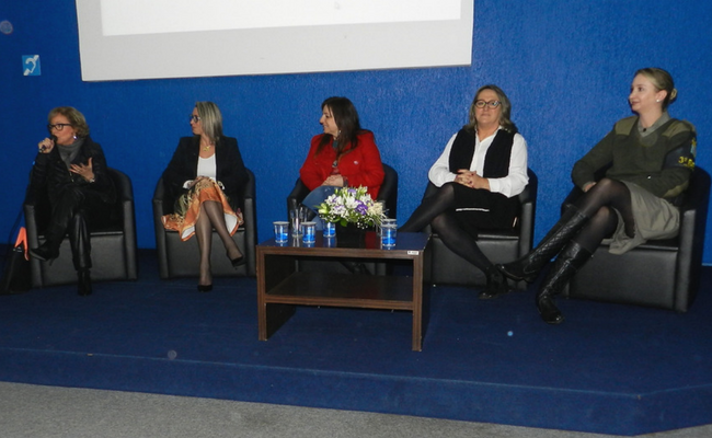 Cinco mulheres sentadas em poltronas em cima de uma palco