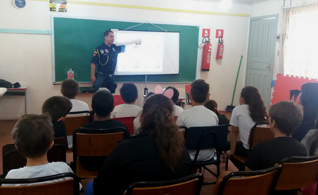 Instrutor em pé em uma sala de aula ao fundo e crianças sentadas