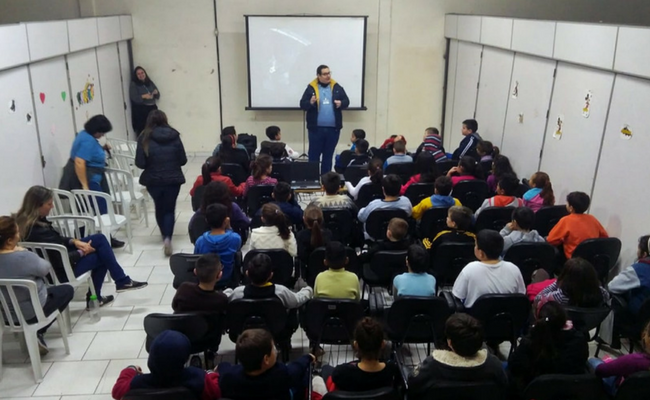 Ao fundo, instrutor em pé e alunos sentados em um auditório