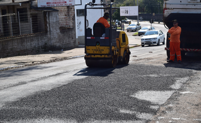 Em uma rua, um máquina com um grande rolo compacta o asfalto