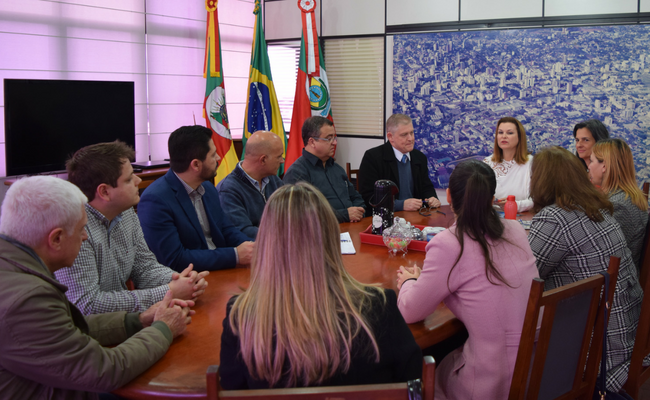 No gabinete, em uma mesa no centro, pessoas sentadas no entorno