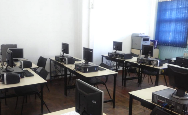 Sala com cinco mesas e monitores de computadores em cima das mesas