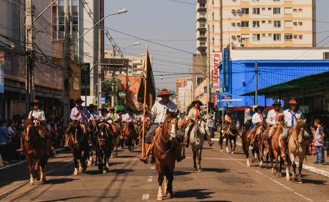 Em uma rua, divididos em três filas, cavaleiros estão montados em cavalos