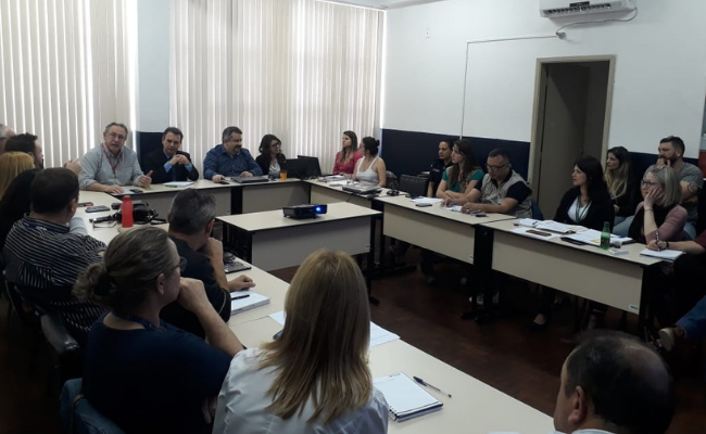 Em um mesa em formato de U, pessoas sentadas ao entorno