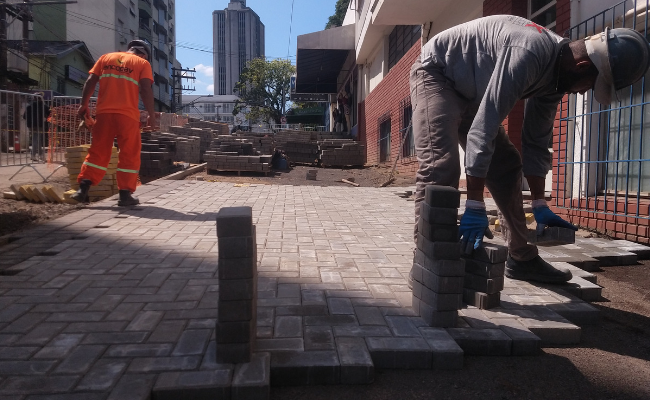 Em uma calçada, dois operários colocando blocos de concretos