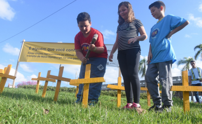 Três crianças colocam cruzes em uma área verde
