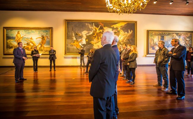 Em pé, à esquerda, o diretor-geral, Márcio Lüders. Os convidados também em pé a sua frente, na Ernesto Frederico Scheffel, um espaço de chão de madeira e quadros expostos nas paredes