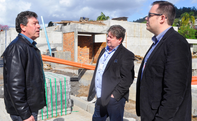 Em pé, três homens com a obra ao fundo