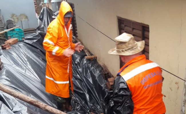Dois homens vestidos de laranja estendem uma lona preta