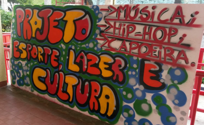 Em uma parede, grafitado colorido o escrito "Projeto esporte, lazar e cultura"