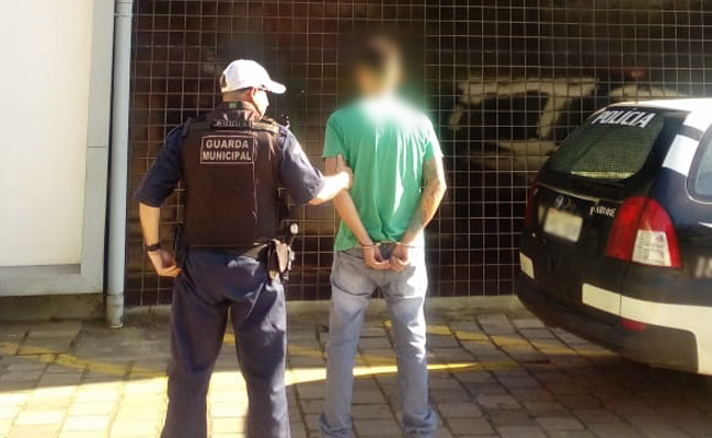 À esquerda, em pé, o Guarda Municipal e a direita, algemado, o preso