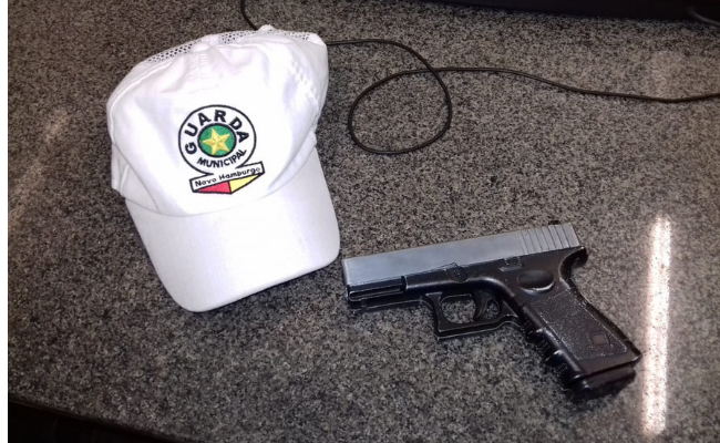 Em uma mesa, o simulacro de pistola e um boné com o símbolo da Guarda Municipal