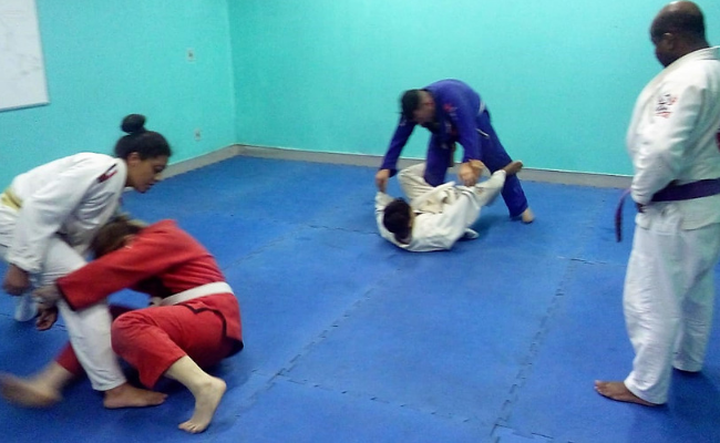 Em um tatâme, quatro alunos lutam sob a supervisão de um professor em pé