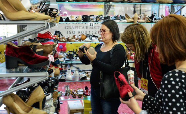Três mulheres olhando uma estande de sapatos