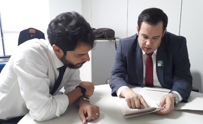 Em uma mesa, sentados, Venturieri e Lüders olhando um documento