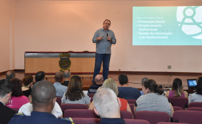 Ao fundo, em cima do palco, General Roberto ao microfone. Platéia sentada à frente