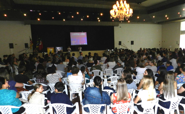 Com um palco ao fundo, participantes do Fórum sentados de frente para este palco