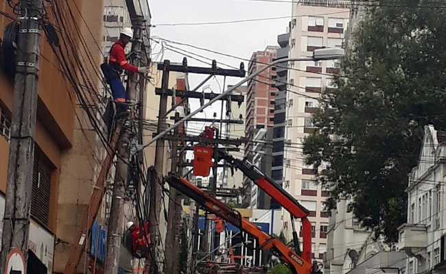 Em uma rua, funcionário de concessionária de energia mexe nos fios de luz em cima de um poste