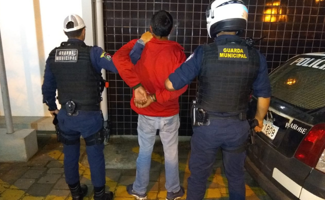 Três homens de costas. Ladrão no meio e dois Guardas Municipais vestidos com o uniforme nos lados
