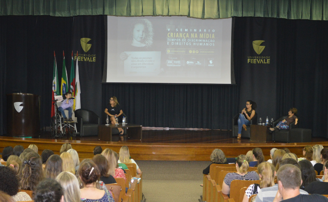 Palco ao fundo com público sentados em cadeiras