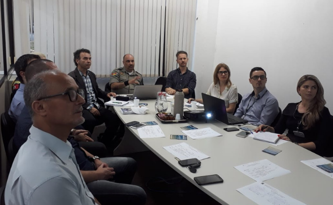 Pessoas sentadas no entorno de uma grande mesa branca ao centro