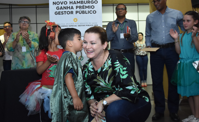 Prefeita agachada e um criança dando-lhe um beijo rosto