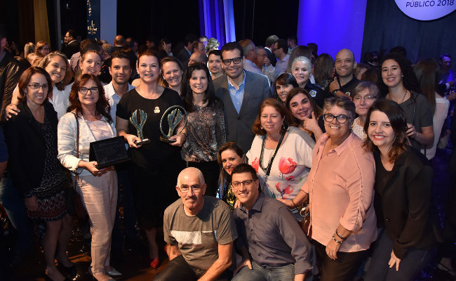 Em um palco, grande grupo de pessoas paradas para a foto