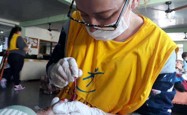 Uma menina vestindo um colete amarelo, máscara e luvas faz as unhas de uma mulher