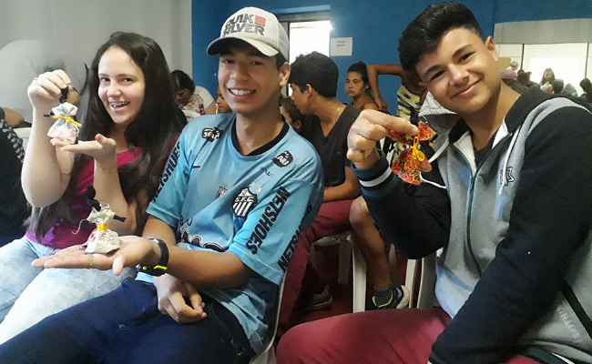 Três alunos sentados mostrando o boneco produzido na atividade