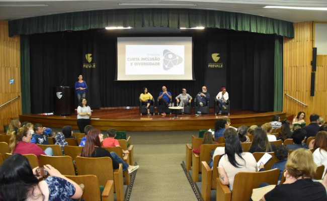 Palco ao fundo com público sentados em cadeiras