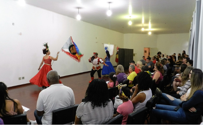 Platéia sentada e dois dançarinos se apresentam à frente