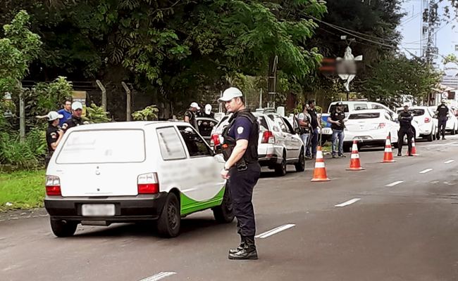 Em uma rua, carro parados em fila e policiais no entorno