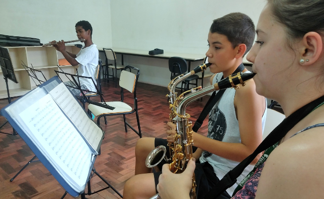 Três crianças sentadas tocando saxofone