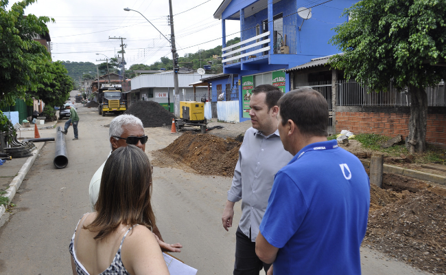 Quatro pessoas em pé e ao fundo a obra em uma rua, com um buraco aberto e canos no chão