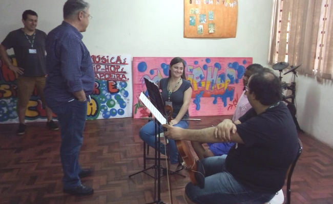 Secretário Roberto, em pé, com três músicos sentados com instrumentos ensaiando