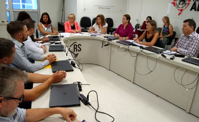 Em uma mesa em formato de U, os prefeitos sentados com a secretária de saúde, Arita Bergmann, na ponta
