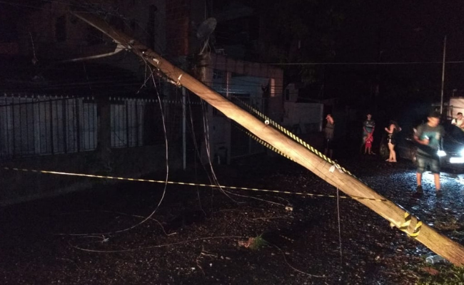 Em uma rua, um poste de energia elétrica caído