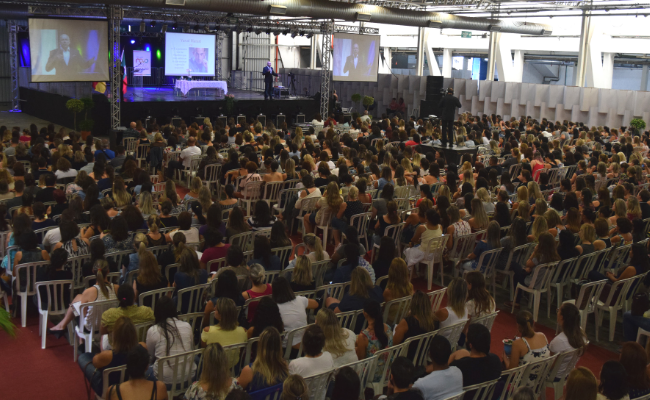 Com um palco ao fundo, participantes do Fórum sentados de frente para este palco