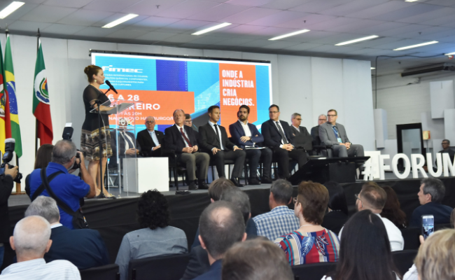 Ao fundo, em um palco, a prefeita Fátima em pé em um pulpito. Autoridades sentados ao lado. Público em frente ao palco sentado